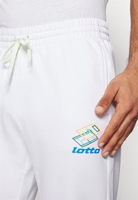 Weiße Sweatpants mit einem elastischen Bund und grünem Kordelzug. Oberschenkel links zeigt ein mehrfarbiges Lotto-Logo-Design.