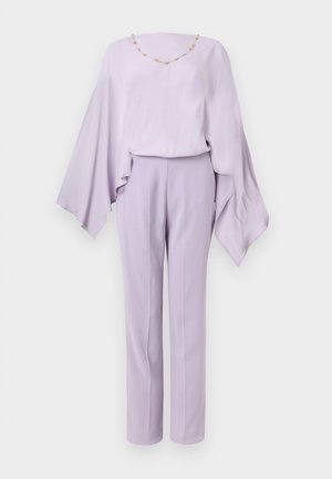 Blouse lilas à manches larges avec détail de collier de perles dorées, associée à un pantalon droit taille haute sur fond blanc.