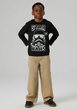 Black long-sleeve shirt with a white Stormtrooper graphic and "STAR WARS" text, paired with beige wide-leg pants and black sneakers.