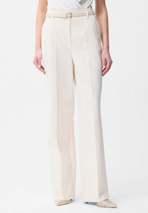 Pantalon large taille haute crème avec ceinture assortie, porté avec des talons blancs tissés à bout pointu.