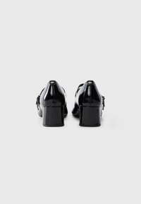 Pair of black patent leather Mary Jane shoes with block heels and buckle straps, shown from the back on a white background.