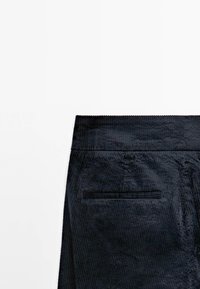 Zwarte corduroy broek met een gestructureerd oppervlak, voorzien van een tailleband en een enkele achterzak met horizontale stiksel details.