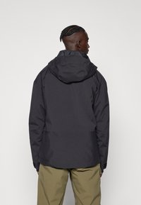 Giacca impermeabile nera con cappuccio aderente, tasche con zip e polsini regolabili. Tessuto con texture, taglio dritto e dettagli delle cuciture.