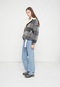 Gray checkered jacket with a cozy lined collar, paired with light blue striped pants. Model stands on a plain background.
