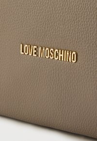 Γκρι δερμάτινη επιφάνεια με υφή, με εμφανές χρυσό λογότυπο "LOVE MOSCHINO" σε μοντέρνα γραμματοσειρά, που τονίζει το σχεδιασμό της μάρκας.