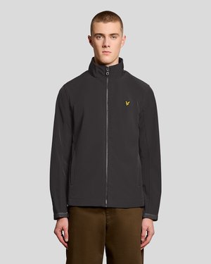 Noor mees, kes kannab musta tõmblukuga jopet kollase linnu logoga ja pruune pükse, seisab ühetaolise helehalli tausta ees.