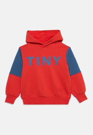 Sweat com capuz vermelho com remendos azuis nas mangas e a palavra "TINY" impressa a azul no peito, apresentada sobre um fundo branco simples.