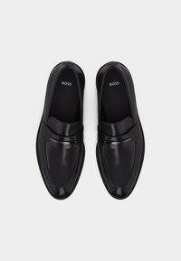 Mocassins en cuir noir à enfiler avec un détail de bande métallique et le logo "BOSS" à l'intérieur et sur la bande, vus de dessus.