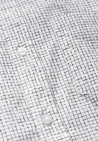 Bílé tričko s černým mřížkovým vzorem, s knoflíkovým zapínáním a hladkou texturou. Obsahuje kapsy a jemné detaily v šití.