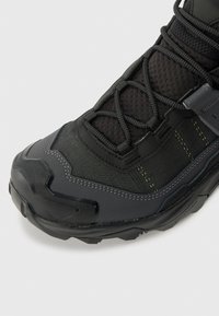 Czarno-szare buty outdoorowe z teksturowaną cholewką, skomplikowanym systemem sznurowania, wzmocnionym czubkiem oraz wytrzymałą, wzorzystą podeszwą.