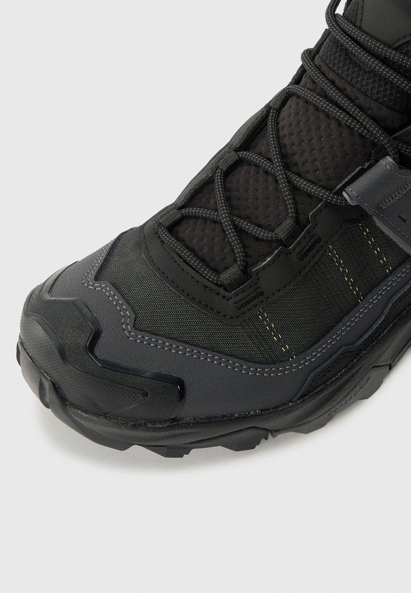 Scarpa da esterno nera e grigia con tomaia testurizzata, sistema di lacci intricato, punta rinforzata e suola robusta e sagomata.