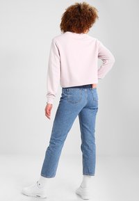 Světle růžová zkrácená mikina s dlouhými rukávy a kulatým výstřihem, v kombinaci se světle modrými rovnými džíny. Bílé tenisky s žebrovanými ponožkami.