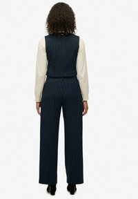 Rompere a righe marinare con un corpino aderente e pantaloni a gamba larga. Presenta una vita cintata e due tasche posteriori. Tessuto dalla consistenza liscia.