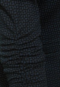Černá a modrá tkanina se vzorem a texturovaným povrchem, obsahující geometrický design a nařasený detail podél švu.
