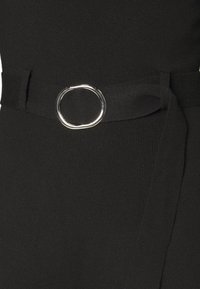 Ceinture en tissu noir avec une boucle ovale argentée lisse attachée autour d'un vêtement noir assorti.