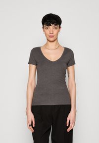 T-shirt gris ajusté à manches courtes et décolleté en V profond, fabriqué dans un matériau doux. La texture semble lisse et extensible.
