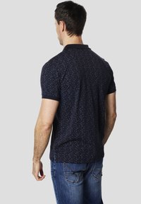 Polo azul marino con un patrón texturizado, de manga corta y con cuello. Combinado con vaqueros azul claro que muestran los bolsillos traseros.