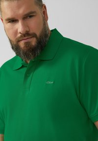 Zielona koszulka polo z teksturowanej tkaniny, z kołnierzykiem i dwoma guzikami, z małym logo s.Oliver po lewej stronie klatki piersiowej.