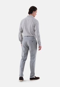 Outfit da uomo con camicia leggera grigia a fantasia con colletto e pantaloni grigi. I pantaloni hanno regolatori laterali e una trama sottile.