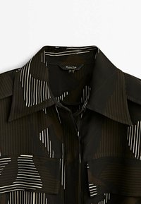 Blusa nera con collo a riviera, caratterizzata da un motivo di strisce e forme organiche in bianco e toni tenui. Include due tasche sul petto.