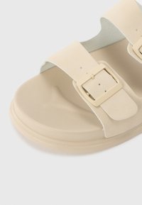 Infradito beige con due fascia larghe e una finitura opaca liscia. Presenta una fibbia rettangolare dello stesso colore. Soletta morbida e suola arrotondata.