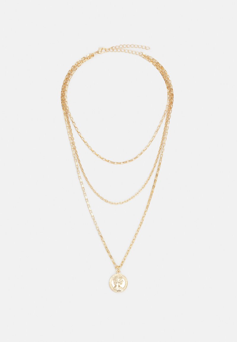 Gold layered necklace featuring three chains of varying lengths, with a circular pendant engraved with a decorative design.