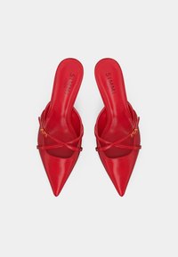 Červené slip-on topánky s úzkymi krížovými remienkami a zlatými prackami, značky SIMMI London, na polstrovaných stielkach.