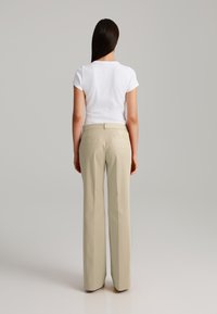 High-waisted beige trousers with a straight leg, dual rear pockets, and a smooth texture. Paired with a white fitted T-shirt.