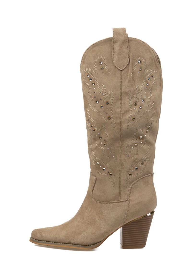 Bota vaquera de ante beige con caña alta, punta afilada, costuras decorativas y adornos metálicos en los laterales. Tacón apilado marrón.