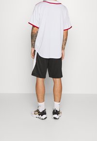 Maglietta atletica bianca con rifiniture rosse, abbinata a pantaloni corti neri. Maniche corte, vestibilità comoda. Sneakers con accenti neri, bianchi e dorati.