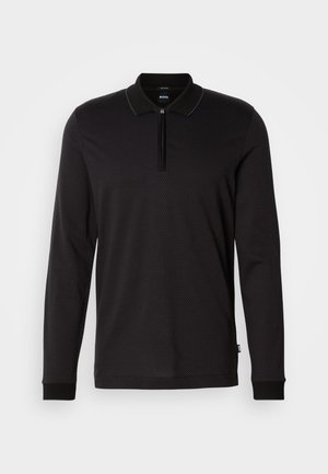 Svart långärmad polotröja med dragkedja i kragen, texturerad tyg med en subtil geometrisk mönstring och kontrasterande manschetter.