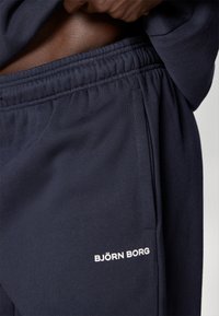 Σκούρο μπλε φόρμες από μαλακό ύφασμα, με ελαστική μέση και πλαϊνές τσέπες. Λογότυπο "BJÖRN BORG" σε λευκό μπροστά.