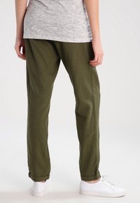 Olive green, loose-fitting trousers made of a soft fabric. Features roll-up cuffs, paired with white sneakers and a gray top.
