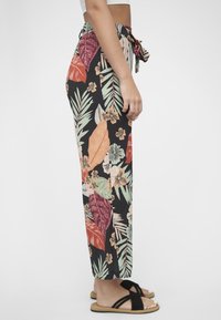 Sorte blomstrete bukser med store, fargerike blad- og blomstermønstre i nyanser av grønt, oransje og rosa, med knyttet midje og avslappet passform.