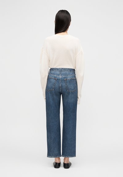 Witte top met lange mouwen, losse pasvorm, gecombineerd met een high-waisted, wijde blauwe spijkerbroek met zichtbare achterzakken en ruwe zoomranden.