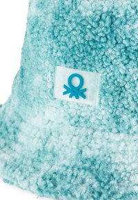 Kapelusz typu bucket w gradientowym odcieniu akwamarynowym, wykonany z pluszowego materiału o miękkiej, teksturowanej powierzchni. Posiada przezroczystą metkę z niebieskim logo ośmiornicy.