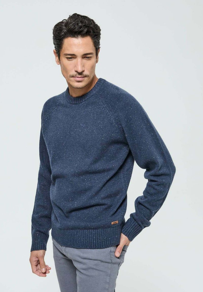 Pull en tricot bleu marine avec un col rond, des poignets et un ourlet côtelés ; présente une texture légèrement mouchetée et une petite étiquette de marque sur le côté.
