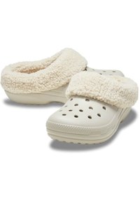 Beige klompen met een zachte, pluche crème-kleurige voering, voorzien van meerdere ventilatiegaten, een lage hak en een gemêleerde buitenzool voor grip.