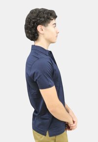 Camicia a maniche corte blu navy con colletto piatto, texture liscia e spacchi laterali. Indossata con pantaloni kaki su uno sfondo neutro.
