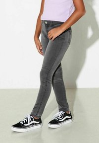 Grå smala jeans i denim, med en klassisk femficksdesign och metallknapp, tillsammans med svarta och vita sneakers.