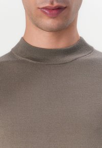 Maglione a collo alto, a coste e color verde oliva, che presenta una trama liscia e un design aderente.