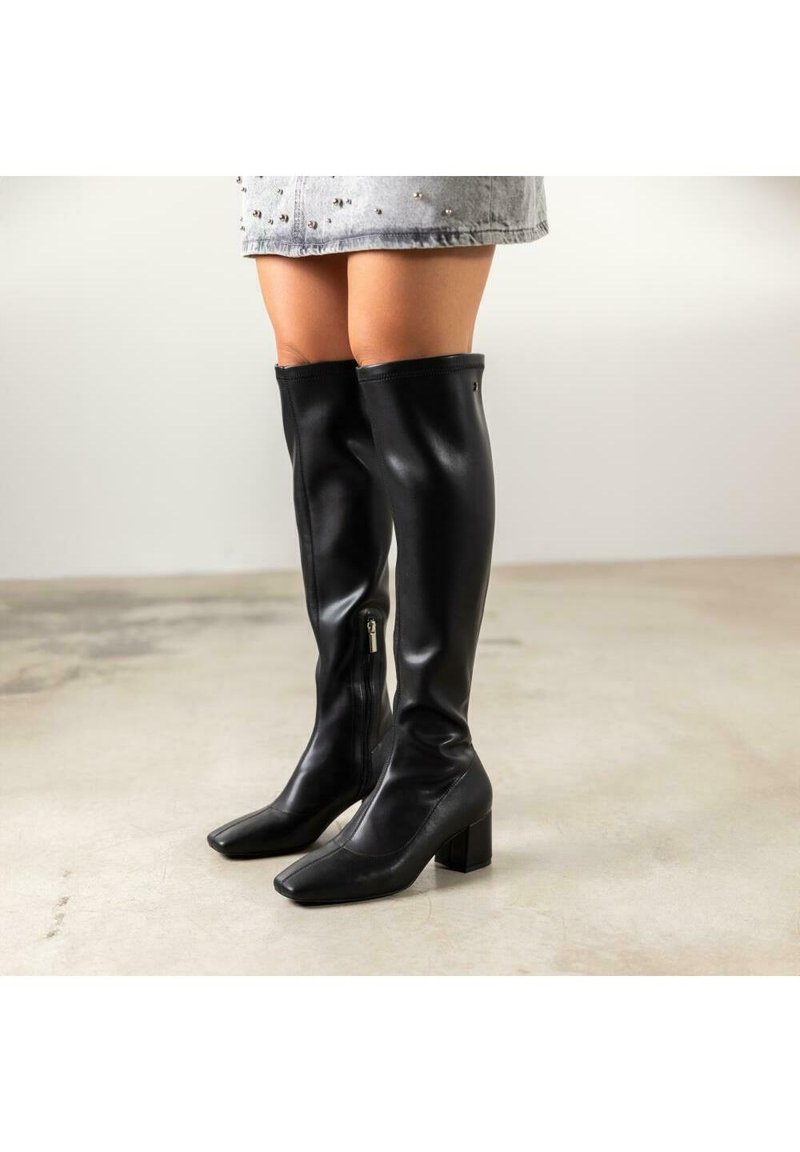 Botas negras por encima de la rodilla hechas de cuero suave con punta cuadrada y tacón bloque; cuentan con una cremallera lateral para facilitar su uso.