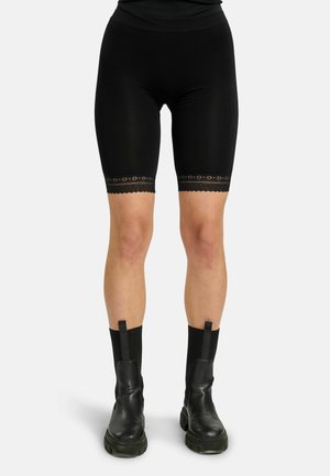 Dolná časť tela v čiernych priliehavých cyklistických krátkych nohaviciach s čipkovaným lemom nad kolenami a čiernych kožených čižmách po stred lýtok s hrubou podrážkou.