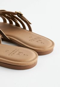 Sandali color tan con più cinturini orizzontali, una tomaia in morbida pelle e una soletta testurizzata. Include un piccolo dettaglio in metallo a forma di fibbia.
