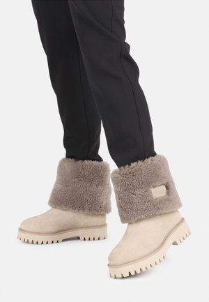 Beige suède enkellaarzen met een fluffy grijze schapenvachtmanchet, een geprofileerde zool met ribbels en een tan accent rond de basis.