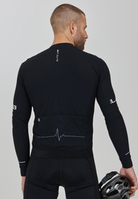 Zwarte lange mouwen fietsjersey met een nauwsluitend ontwerp, subtiele hartslagpatroon op de achterkant en reflecterende branding op de mouwen.