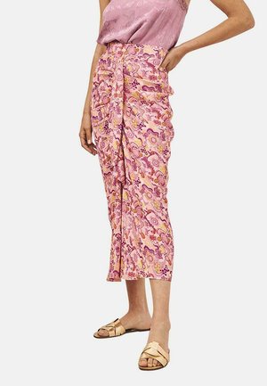 Falda envuelta de color rosa con estampado y volantes, que presenta remolinos y acentos florales. Hecha de una tela ligera, combinada con una blusa lavanda y sandalias.