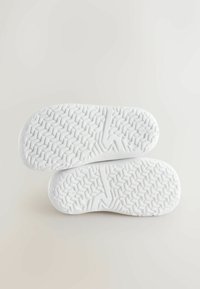 White sneaker soles with a textured, herringbone pattern. Features rounded edges and a minimalist design with embossed logo detail.