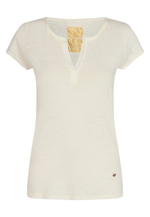 Chemise courte pour femme de couleur crème avec un col en V arrondi et un petit logo métallique circulaire près de l'ourlet inférieur.