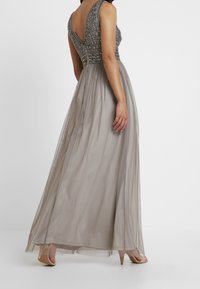 Maxi dress in grey with a V-back, embellished bodice, and sheer flowing skirt. Includes subtle textures and a fitted waist.